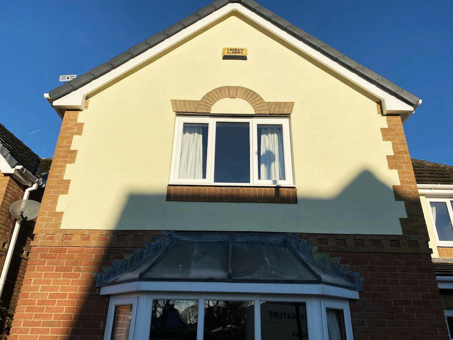 single white casement window in the centre of a cream house with a small brick arch in the wall.